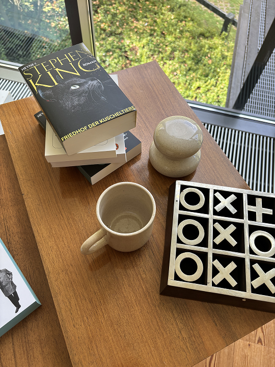 Tasse, Dose und Bücher auf einem Holztisch mit einem Tic-Tac-Toe Spiel